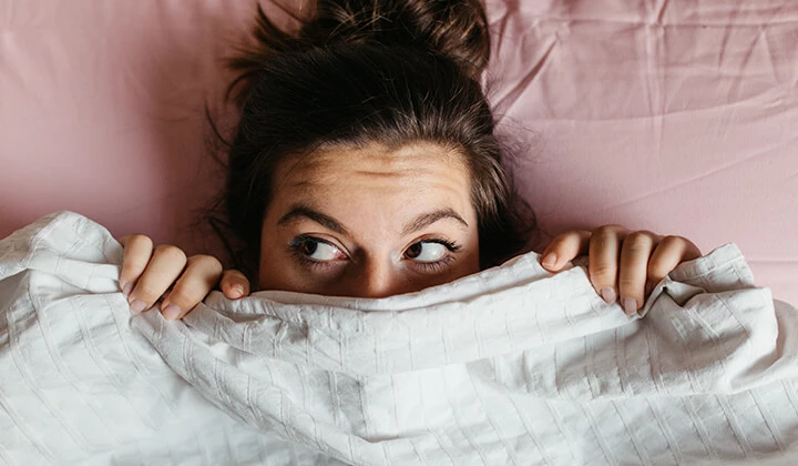 Frau versteckt sich unter Bettdecke Frau mit Angst vorm Schlafen unter der Bettdecke