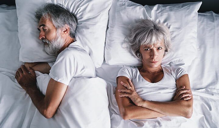 Frau liegt schlaflos im Bett neben schnarchendem Mann Frau liegt schlaflos im Bett neben schnarchendem Mann