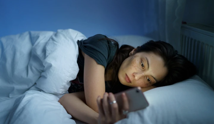 Frau mit Einschlafstörung Frau mit Handy im Bett