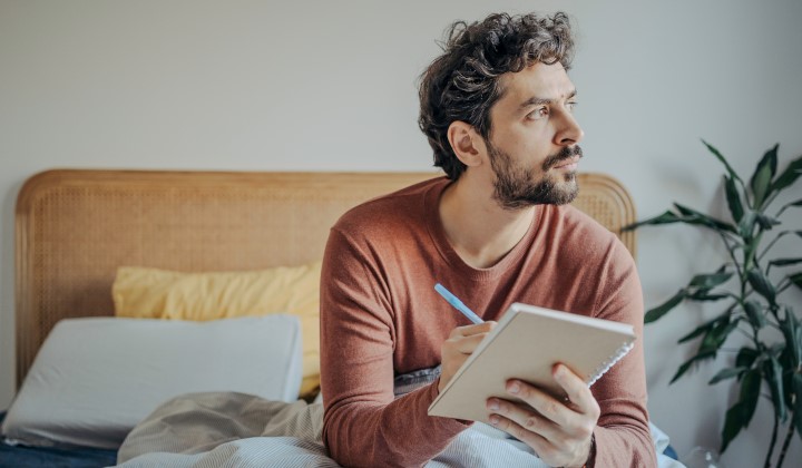 Mann sitzt im Bett und führt Schlaftagebuch Mann sitzt im Bett und führt Schlaftagebuch